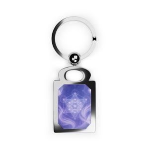 May include: A silver-colored keychain with a rectangular pendant featuring a geometric design on a blue and purple background. The keychain has a circular ring and a small, decorative element connecting the ring to the pendant.