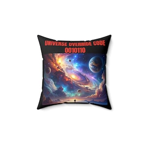 Może przedstawiać: Czarna kwadratowa poduszka z żywą kosmiczną sceną: wirujące mgławice, planety i samotna postać. Tekst "UNIVERSE OVERRIDE CODE 0010110" jest wydrukowany na czerwono. Dekoracyjny akcent dla entuzjastów kosmosu.