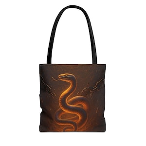 May include: A tote bag with a black handle and a dark brown background. The bag features a golden snake illustration with a forked tongue. The snake is coiled and surrounded by chains, creating a mystical theme.