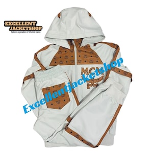 May include: White tracksuit with brown MCM logo accents. The jacket has a hood and a zipper closure. The pants have a pocket with the MCM logo. The text "Excellent Jacketshop" is visible.