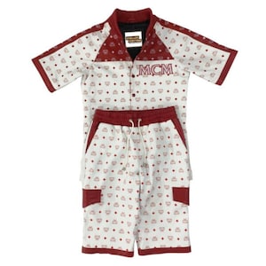 May include: White and red short-sleeved shirt and shorts set. The shirt has a red collar and sleeves, with the letters "MCM" on the front. The set is patterned with small red logos. The shorts have a drawstring and red pockets.
