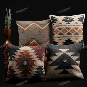 Könnte beinhalten: Vier quadratische dekorative Kissen mit geometrischen Mustern in Braun-, Schwarz- und Cremetönen. Die Kissen sind in einer Gruppe angeordnet und zeigen ihre verschiedenen Designs und Texturen. Im Hintergrund eine hohe braune Vase mit einer Pflanze.