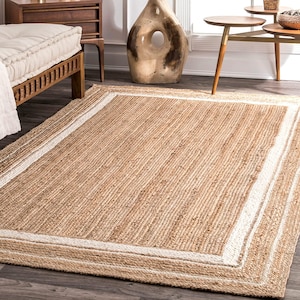 May include: A rectangular jute rug with a natural tan color and a white border. The rug has a woven texture and is suitable for indoor use. The rug is a neutral color and can be used in a variety of rooms.