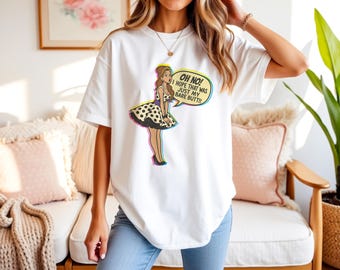 May include: White t-shirt featuring a cartoon illustration of a woman in a polka dot dress and the text "OH NO! I HOPE THAT WAS JUST MY BARE BUTT!!" The design has a retro comic book style.