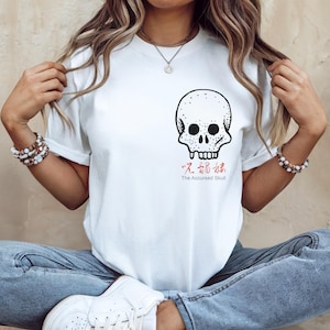 以下が含まれることがあります： 黒いスカルグラフィックと、アジアの文字で「The Accursed Skull」と書かれた赤い文字が特徴の白いTシャツ。 スカルのデザインは胸の中央にあります。