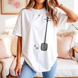 May include: White t-shirt with a black and grey illustration of an erhu, a traditional Chinese instrument. The shirt also features Chinese characters. The t-shirt is being worn by a person.