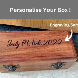 May include: A rectangular wooden box with a dark brown finish, featuring metal clasps and hinges. The box is engraved with the text "Jody M. Kole 2022". The image also includes the text "Personalise Your Box !" and "Engraving Sample".