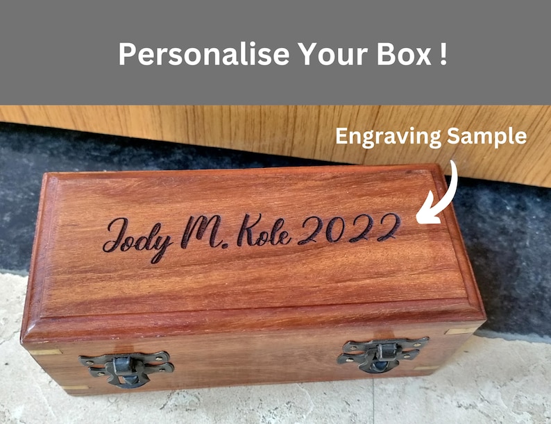 May include: A rectangular wooden box with a dark brown finish, featuring metal clasps and hinges. The box is engraved with the text "Jody M. Kole 2022". The image also includes the text "Personalise Your Box !" and "Engraving Sample".