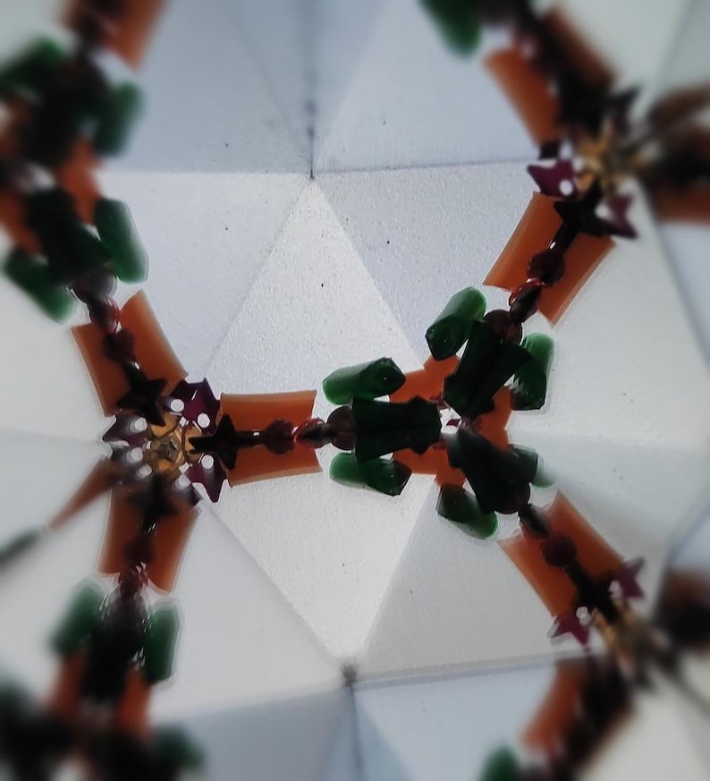 May include: Abstract kaleidoscope image with a geometric pattern. The design features orange, green, and burgundy elements arranged around a central point. The background is a light, geometric shape, creating a symmetrical and colorful visual.