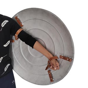 Pu&ograve; includere: Uno scudo circolare argentato con anelli concentrici e cinghie in pelle marrone. Lo scudo ha una finitura metallica ed &egrave; progettato per la protezione. Le cinghie sono rivettate allo scudo per una presa sicura.
