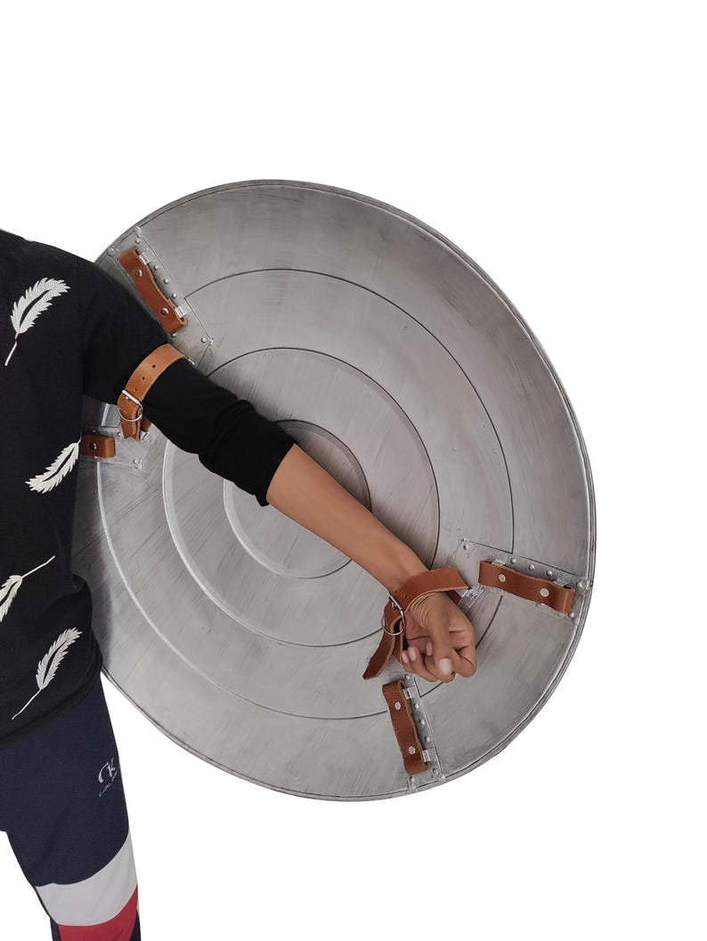 Pu&ograve; includere: Uno scudo circolare argentato con anelli concentrici e cinghie in pelle marrone. Lo scudo ha una finitura metallica ed &egrave; progettato per la protezione. Le cinghie sono rivettate allo scudo per una presa sicura.