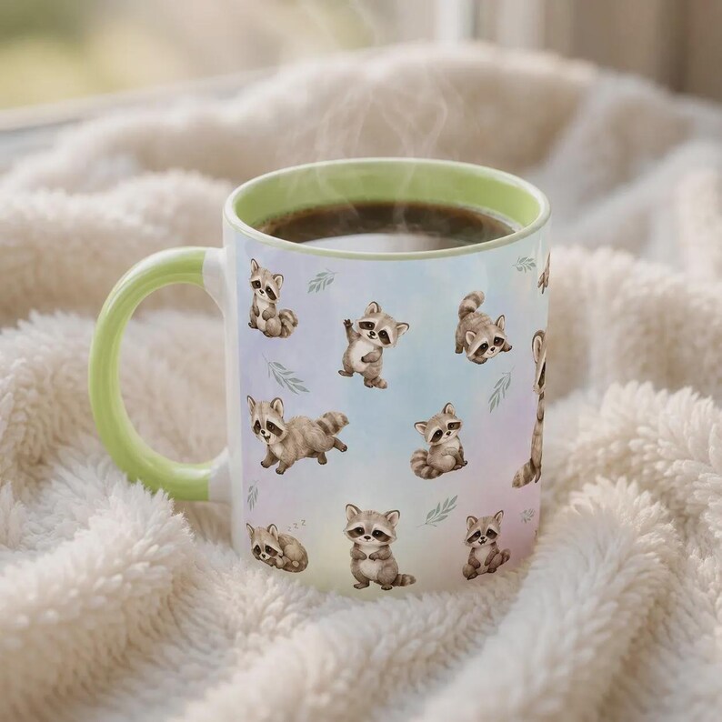 May include: A ceramic mug with a light green handle and rim, featuring a repeating pattern of small, illustrated raccoons in various poses against a soft, pastel-colored background. The mug is filled with a dark brown liquid, emitting a faint steam.