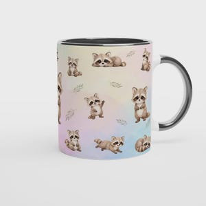May include: A ceramic mug with a black interior and handle, featuring a repeating watercolor-style pattern of small brown and grey raccoons in various poses, including sitting, standing, and lying down, set against a soft pastel gradient background.
