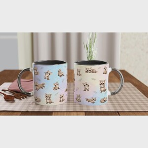 May include: Two ceramic mugs featuring a repeating pattern of small, illustrated raccoons in various poses against a soft, pastel-colored gradient background. Each mug has a black handle and a black interior rim, showcasing a whimsical animal design.