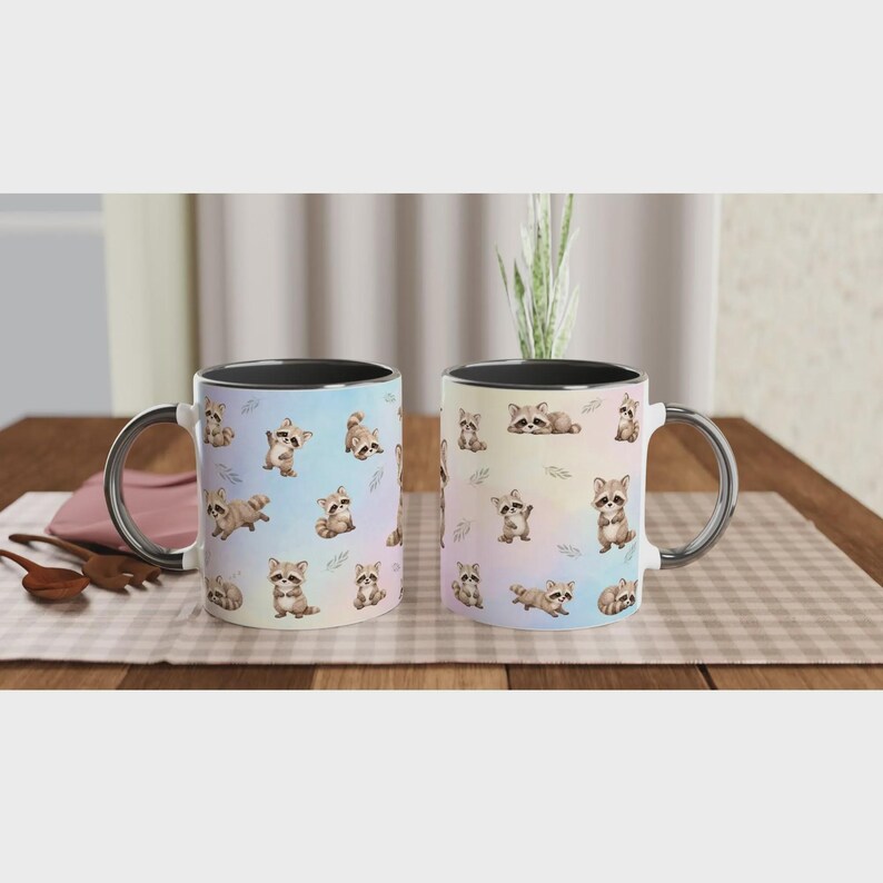May include: Two ceramic mugs featuring a repeating pattern of small, illustrated raccoons in various poses against a soft, pastel-colored gradient background. Each mug has a black handle and a black interior rim, showcasing a whimsical animal design.