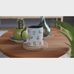 May include: A ceramic mug with a black interior and handle, featuring a repeating pattern of small, illustrated brown and grey raccoons on a light blue background. The mug is cylindrical with a smooth finish and a black rim.
