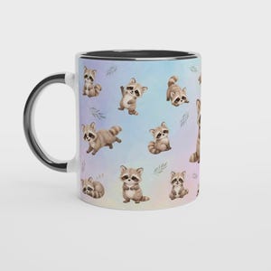 May include: A ceramic mug with a black handle and interior, featuring a repeating pattern of illustrated brown and grey raccoons in various poses against a soft, pastel-colored watercolor background with small green leaf accents.