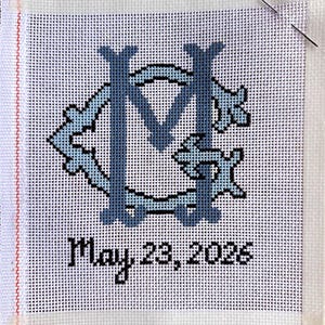 Peut inclure: Toile de canevas avec un monogramme bleu clair et foncé. Le motif présente les lettres "M" et "C" entrelacées avec des éléments décoratifs. La date "May 23, 2026" est brodée en dessous du monogramme.