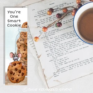 May include: A whimsical bookmark featuring a cartoon mouse holding a large chocolate chip cookie. The bookmark reads "You're One Smart Cookie" and includes a jar of cookies. A cup of coffee and a vintage book are also in the image.