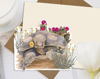 May include: A desert tortoise with a brown shell and a pink cactus on its back. The tortoise is surrounded by yellow flowers and green plants.