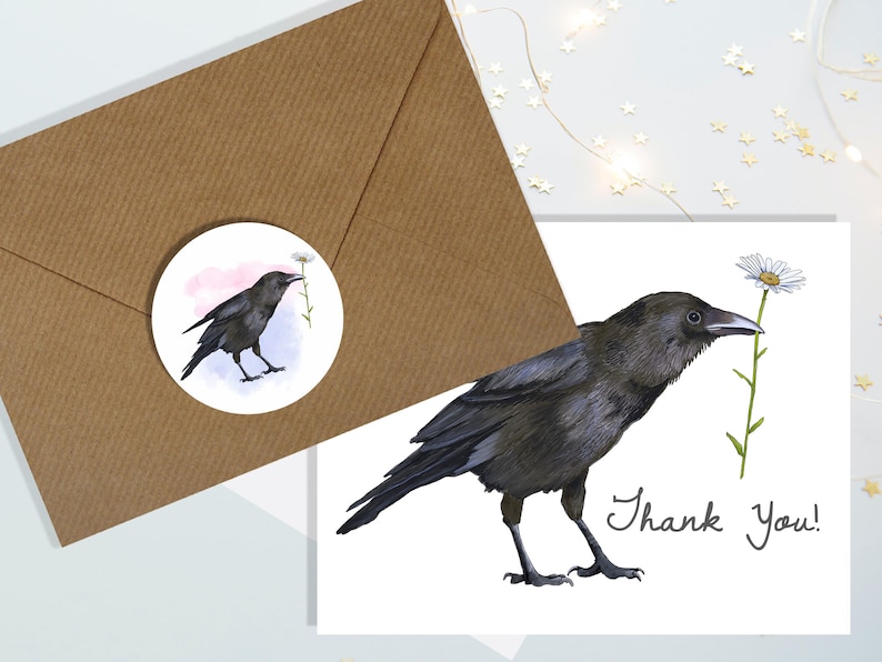May include: A watercolour illustration of a black crow holding a daisy, with the words "Thank You!" on a white card. A matching sticker and a brown envelope are also present. The crow is the focal point, with detailed feathers and a delicate flower.