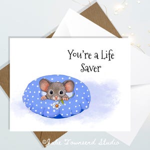 May include: A greeting card with a blue and white polka dot background. A small mouse with brown fur is peeking out of a blue and white polka dot ring. The text "You're a Life Saver" is written in black on the card.