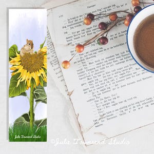 May include: A watercolor bookmark featuring a yellow sunflower with a small brown and white squirrel perched on the sunflower. The background is a light blue sky with green grass at the bottom.
