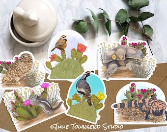 May include: A collection of die-cut stickers featuring desert wildlife. The stickers depict a burrowing owl, a bird on a cactus, a tortoise, a chipmunk, a quail, and a Gila monster. The stickers are surrounded by desert plants and flowers. The artist's name, "Julie Townsend Studio", is printed on the bottom.
