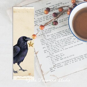 May include: A bookmark featuring a watercolor illustration of a black raven with a gold star. The bookmark is set against a vintage book page and a cup of coffee. The text "Julie Townsend Studio" is at the bottom.