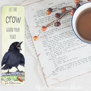 May include: A bookmark with a watercolor illustration of a black crow perched on books, with the text "LET THE CROW GUARD YOUR PLACE." The bookmark is on a book page with a cup of coffee and berries.