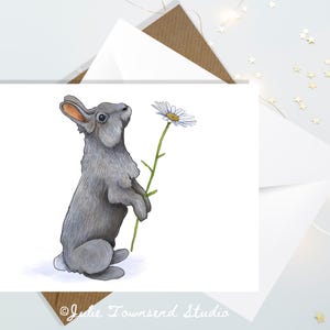 May include: A gray rabbit holding a white daisy with a yellow center. The rabbit is standing on its hind legs and looking up at the flower. The background is white.