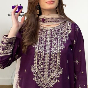 May include: A deep purple embroidered tunic and scarf set. The tunic features intricate gold floral embroidery down the front and on the sleeves. The scarf is a light beige color with a matching embroidered border. The brand name "MA Kyara" is visible in the top left corner.