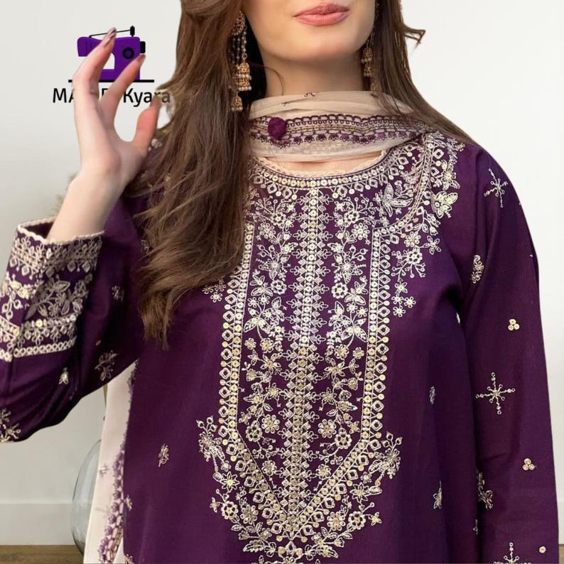 May include: A deep purple embroidered tunic and scarf set. The tunic features intricate gold floral embroidery down the front and on the sleeves. The scarf is a light beige color with a matching embroidered border. The brand name "MA Kyara" is visible in the top left corner.