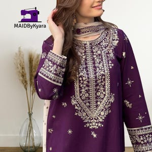 May include: A deep purple embroidered tunic and scarf set. The tunic features intricate gold floral embroidery along the neckline, sleeves, and bodice. The scarf has matching embroidery. The logo "MAIDByKyara" is in the top left corner.