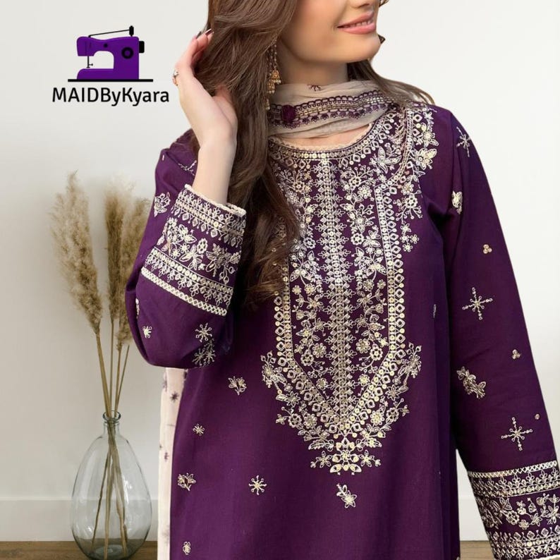 May include: A deep purple embroidered tunic and scarf set. The tunic features intricate gold floral embroidery along the neckline, sleeves, and bodice. The scarf has matching embroidery. The logo "MAIDByKyara" is in the top left corner.