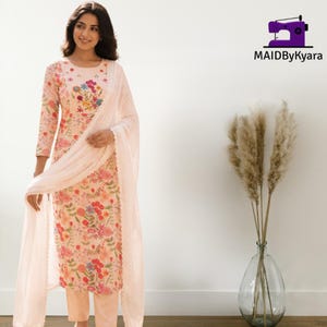 May include: A light peach-colored long-sleeved tunic and matching trousers featuring a vibrant floral print with red, pink, yellow, and green flowers. A sheer, solid light peach-colored dupatta scarf is draped over the shoulders and arms.