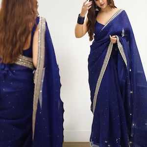 May include: A navy blue saree with a shimmering border and scattered embellishments. The fabric drapes elegantly, featuring a deep V-neckline. The saree's design includes a subtle sparkle, adding a touch of glamour to the traditional garment. The saree is a traditional Indian garment.
