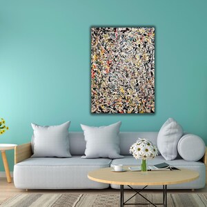 Puede incluir: Pintura expresionista abstracta con fondo negro y salpicaduras de colores. La obra de arte cuelga sobre un sofá gris con cojines blancos. Una mesa de centro redonda de madera y una mesita auxiliar con flores están frente al sofá.