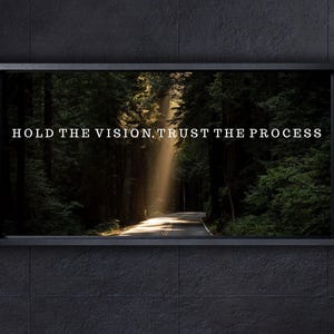 Könnte beinhalten: Gerahmtes Wandbild mit einer sonnendurchfluteten Waldstraße. Der Text "HOLD THE VISION. TRUST THE PROCESS" ist in Weiß geschrieben. Das Kunstwerk hängt an einer dunkelgrauen gefliesten Wand.
