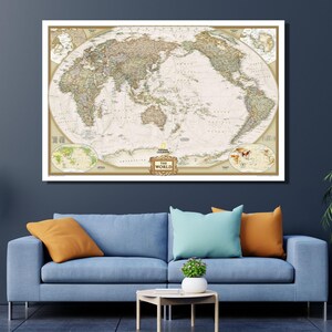 May include: A framed vintage world map with a cream-colored background and detailed geographical features. The map is in a white frame and includes the text "THE WORLD". The map is displayed above a blue sofa with colorful pillows.