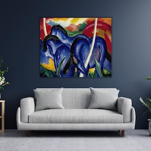 Può includere: Un dipinto astratto di tre cavalli blu con criniere e code nere, su uno sfondo vibrante di rosso, giallo e verde. L'opera d'arte è esposta sopra un divano grigio.