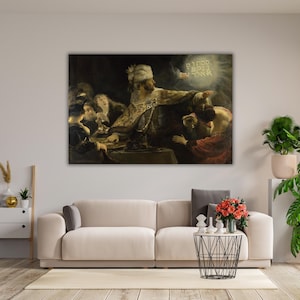 May include: A large framed painting depicting a historical scene with several figures. The central figure, wearing ornate clothing, points towards a glowing inscription. The artwork is displayed above a beige sofa, complemented by potted plants and a modern coffee table.