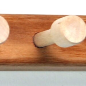 Puede incluir: Un perchero de pared de madera con seis clavijas de madera. El perchero est&aacute; hecho de madera marr&oacute;n claro con una mancha marr&oacute;n m&aacute;s oscura. Las clavijas son de color madera natural claro.
