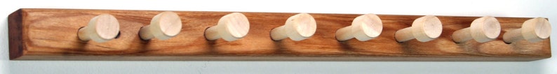 Puede incluir: Un perchero de pared de madera con seis clavijas de madera. El perchero est&aacute; hecho de madera marr&oacute;n claro con una mancha marr&oacute;n m&aacute;s oscura. Las clavijas son de color madera natural claro.
