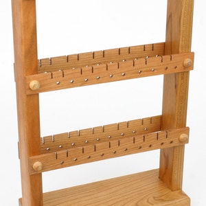 May include: A wooden earring holder with three tiers of holes for storing earrings. The holder is made of light brown wood and has a simple, rustic design.