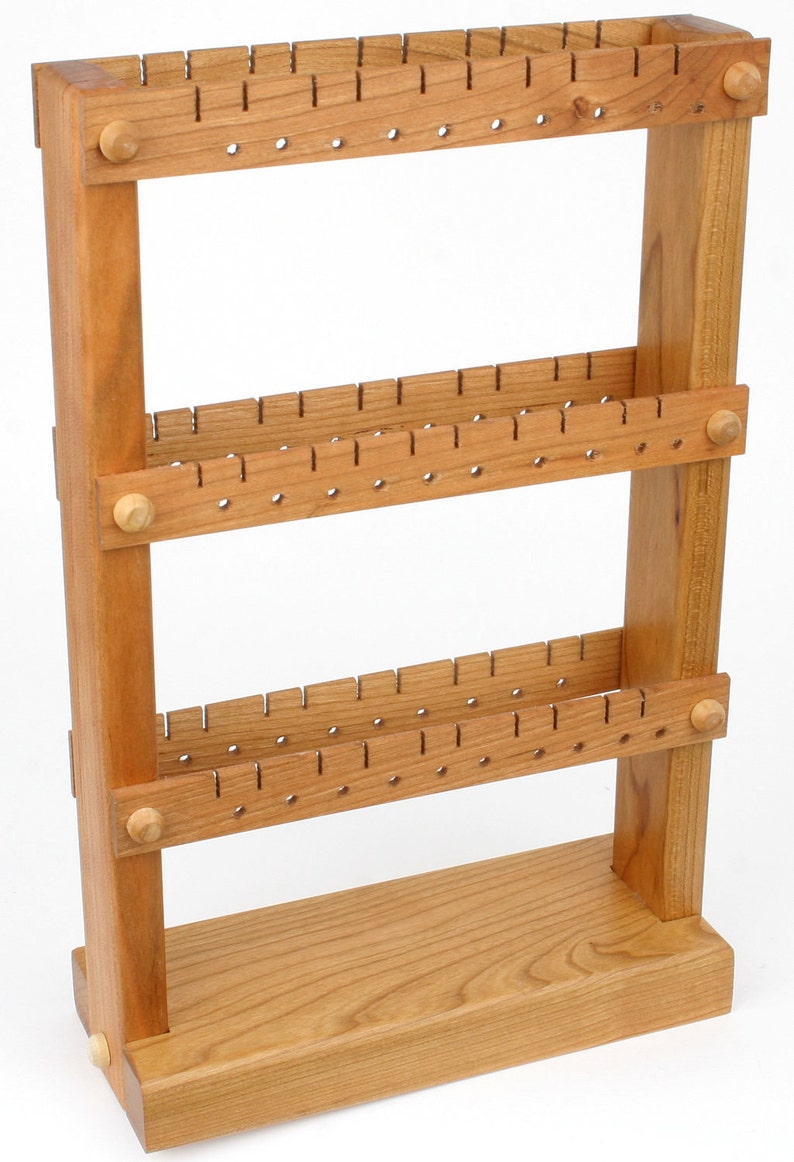 May include: A wooden earring holder with three tiers of holes for storing earrings. The holder is made of light brown wood and has a simple, rustic design.