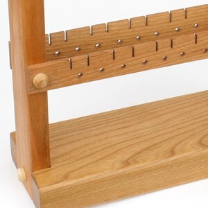 May include: A wooden earring display stand with two rows of holes for earrings. The stand is made of light brown wood and has a simple design.