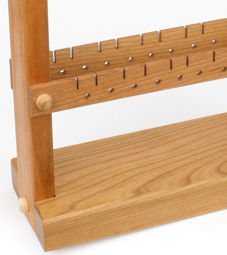 May include: A wooden earring display stand with two rows of holes for earrings. The stand is made of light brown wood and has a simple design.