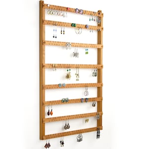 Puede incluir: Un soporte para pendientes de madera con múltiples filas de clavijas para colgar pendientes. El soporte está hecho de madera natural y tiene un aspecto rústico. Es una excelente manera de organizar y exhibir tu colección de pendientes.