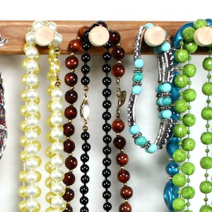 Puede incluir: Un estante de madera para joyas con varios collares y pulseras colgando de &eacute;l. Los collares est&aacute;n hechos de varios materiales, incluyendo perlas, cuentas y turquesa. Las pulseras est&aacute;n hechas de metal y turquesa.